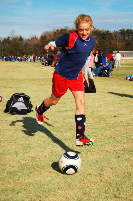 Maggie running in a blue red uniform getting ready to kick the ball in a game.