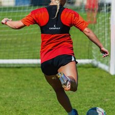 women soccer player wearing GPS tracker and kicking a soccer ball into the goal.