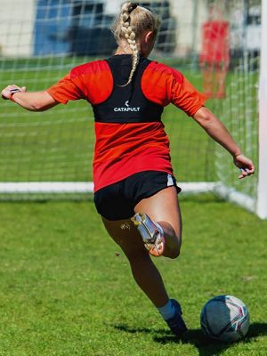 women soccer player wearing GPS tracker and kicking a soccer ball into the goal.