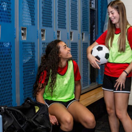 Two soccer teammates in a locker room smiling together after soc