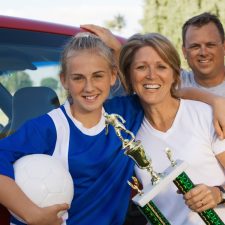 High School Girl on College Recruiting Trip with Parents in front of car by soccer field