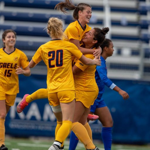 Christie Gray, in yellow Queen's University uniform jumping up into the arms of her teammates.