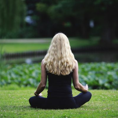 meditation, mindfulness, nature woman sitting in front of pond on grass.